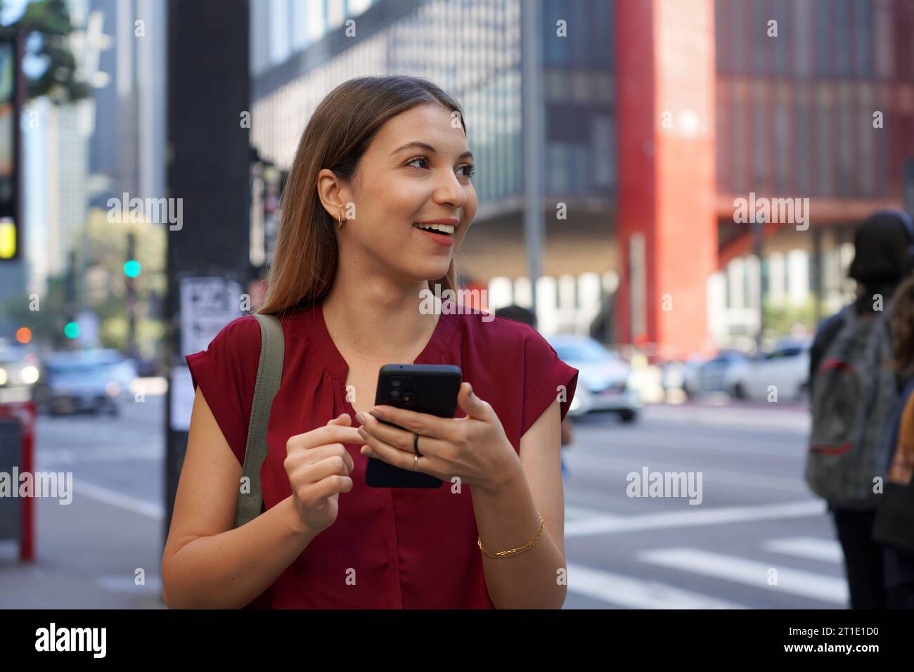 Primo piano di una donna d'affari brasiliana saluta un veicolo utilizzando un'app mobile che guarda sul lato di Paulista Avenue, San Paolo, Brasile Foto Stock