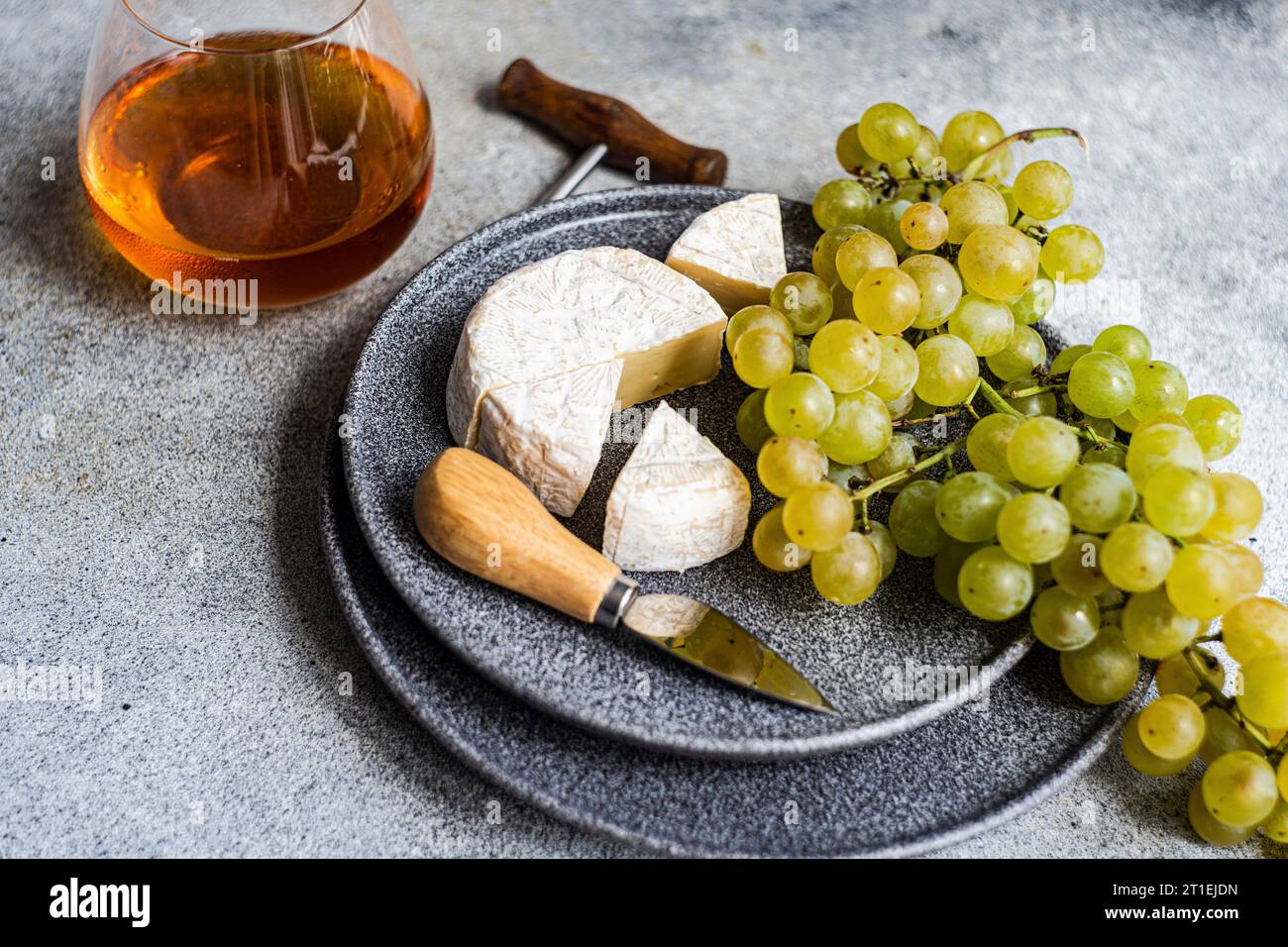 Brie e uva verde su piatto di pietra e un bicchiere di vino bianco Foto Stock