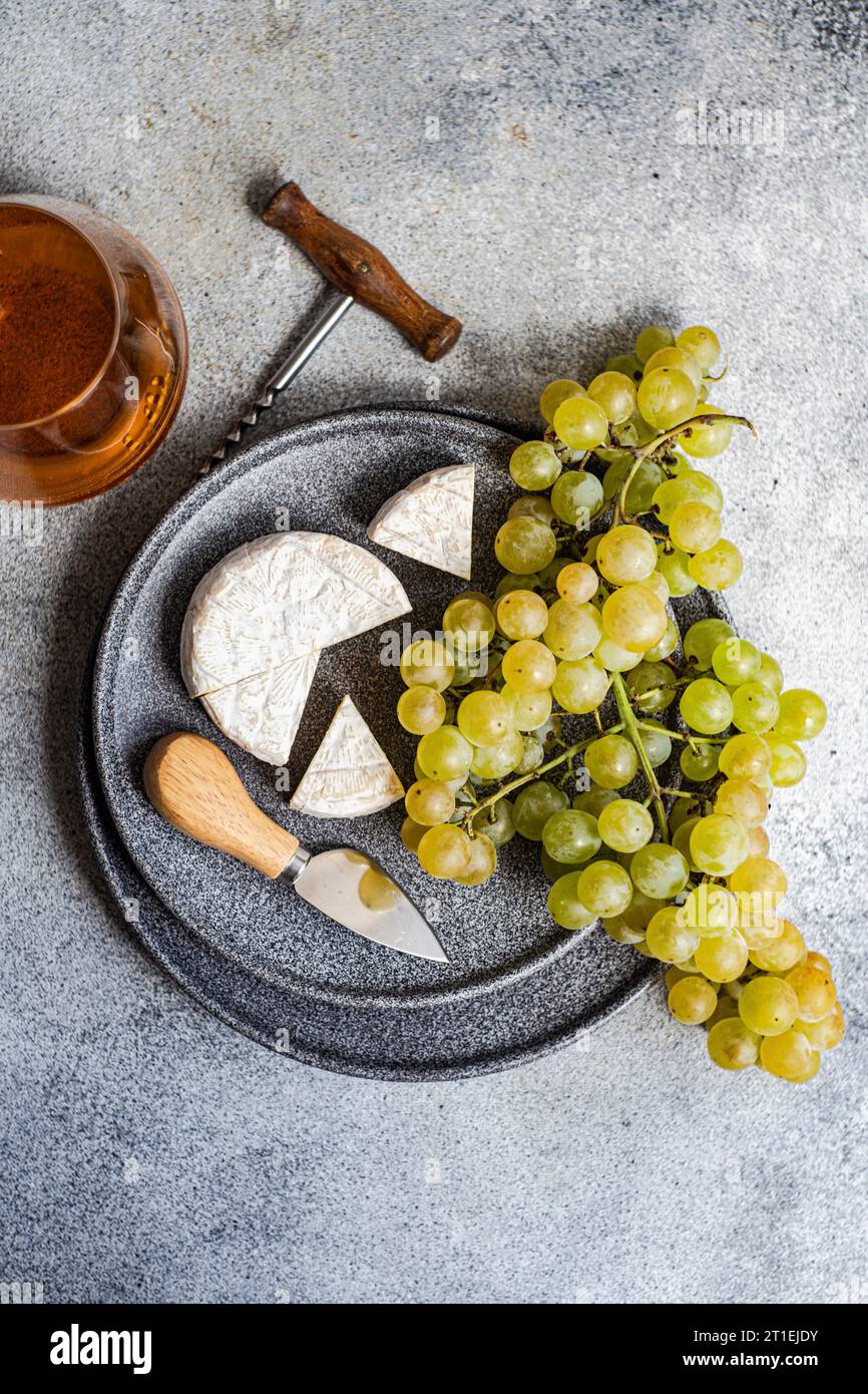 Brie e uva verde su piatto di pietra e un bicchiere di vino bianco Foto Stock