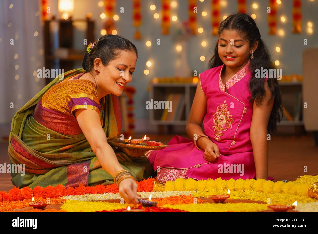 Nonna felice con la nipote di una ragazza che posiziona lampade diya sui rangoli di fiori - concetto di preparazione del festival diwali, rituale tradizionale o usanza e. Foto Stock