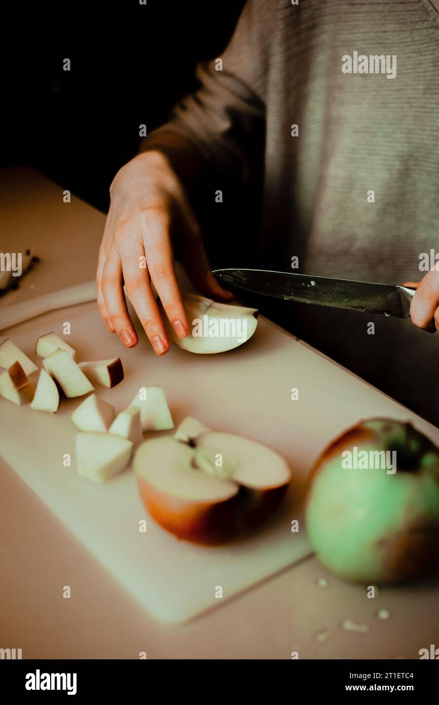 Una donna che affetta sapientemente mele mature con un coltello. Descrive il tema della cucina casalinga in cucina e sottolinea l'importanza della frutta e. Foto Stock