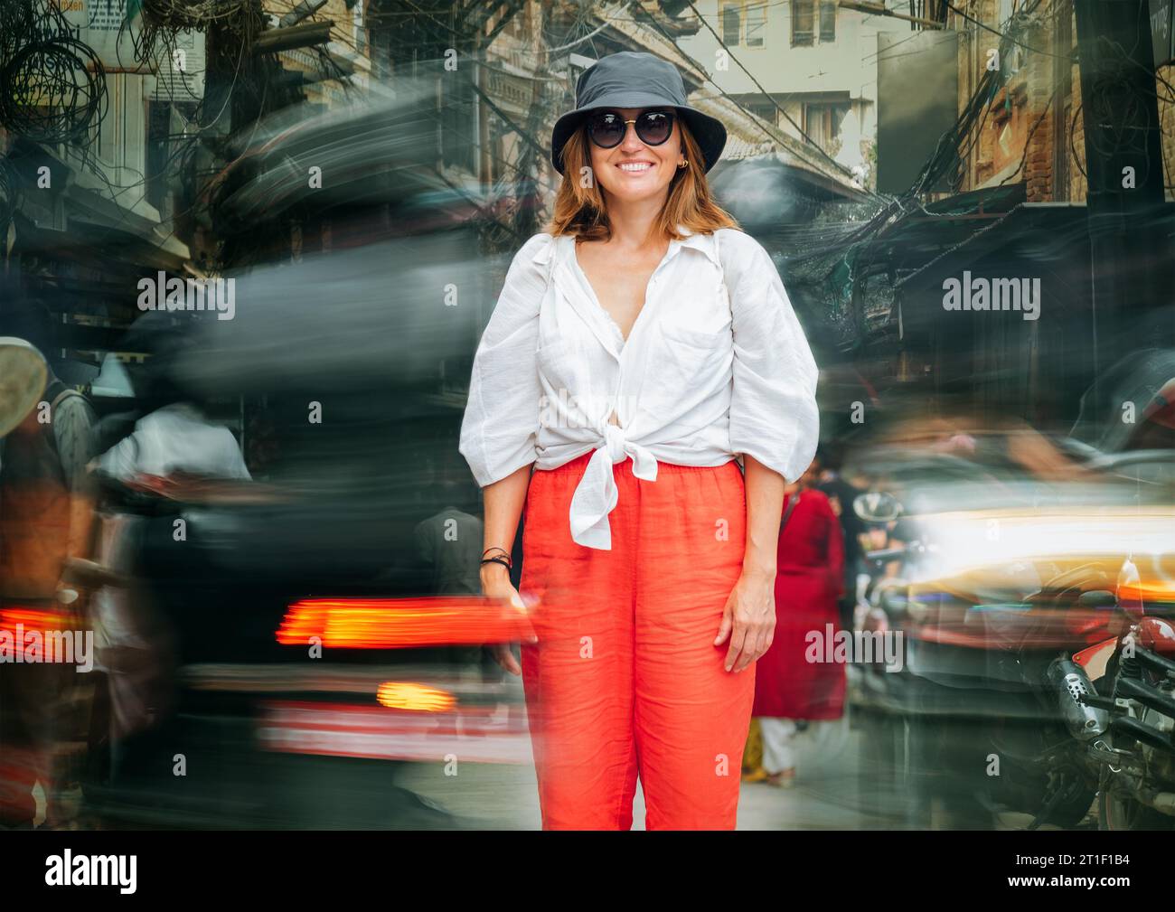 Una simpatica turista sorridente che si trova sulla stretta strada nepalese di corsa all'interno del traffico cittadino in rapido movimento con auto, moto e risciò. T Foto Stock