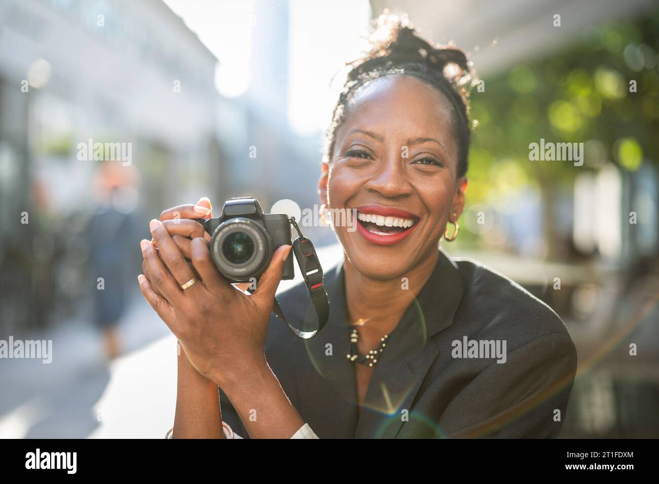 Ritratto di una donna sorridente che tiene una macchina fotografica in città Foto Stock