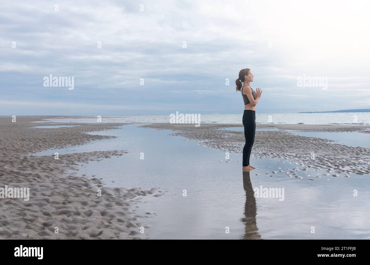Donna che medita sulla costa con la bassa marea, luce soffusa. Allontanarsi da tutto. Foto Stock