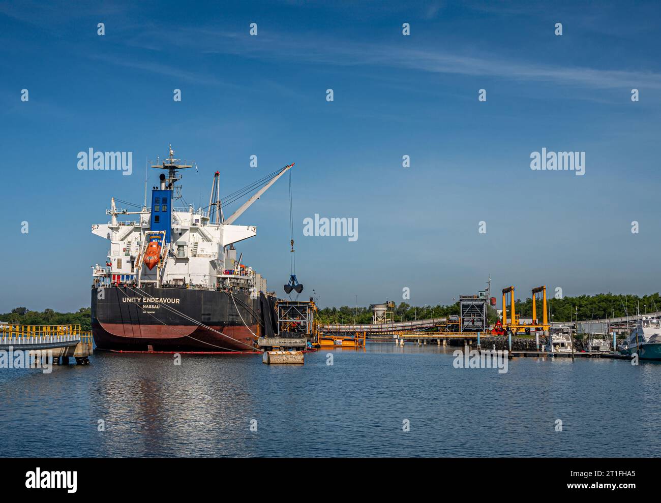 Guatemala, Puerto Quetzal - 20 luglio 2023: La portacontainer Unity Endeavour scarica carbone al terminal sotto il cielo blu. Impianti industriali di gru e. Foto Stock