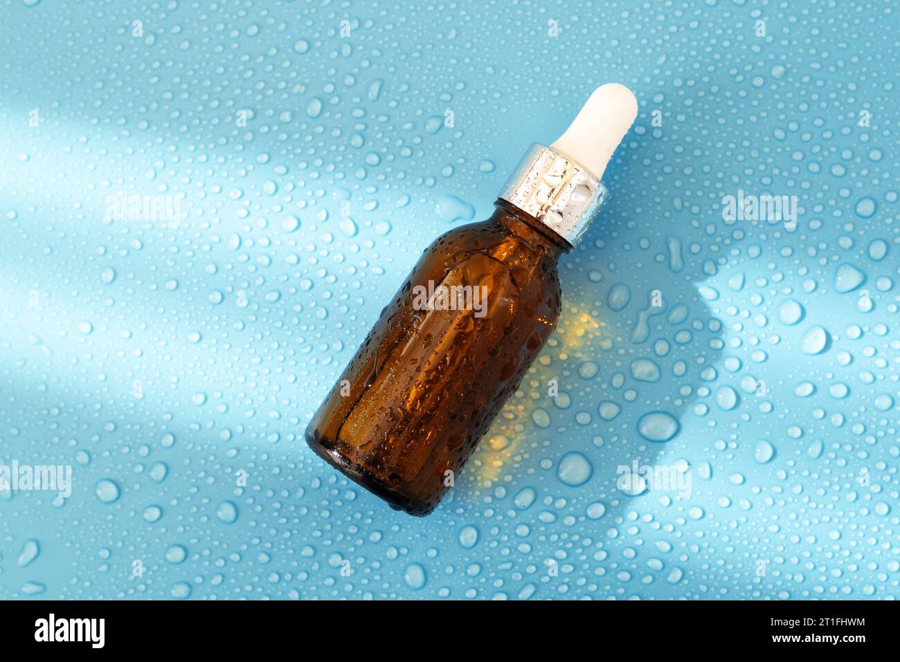 Flacone per siero , olio cosmetico su sfondo blu con luce dura e gocce d'acqua. con ombreggiatura piatta, vista superiore Foto Stock