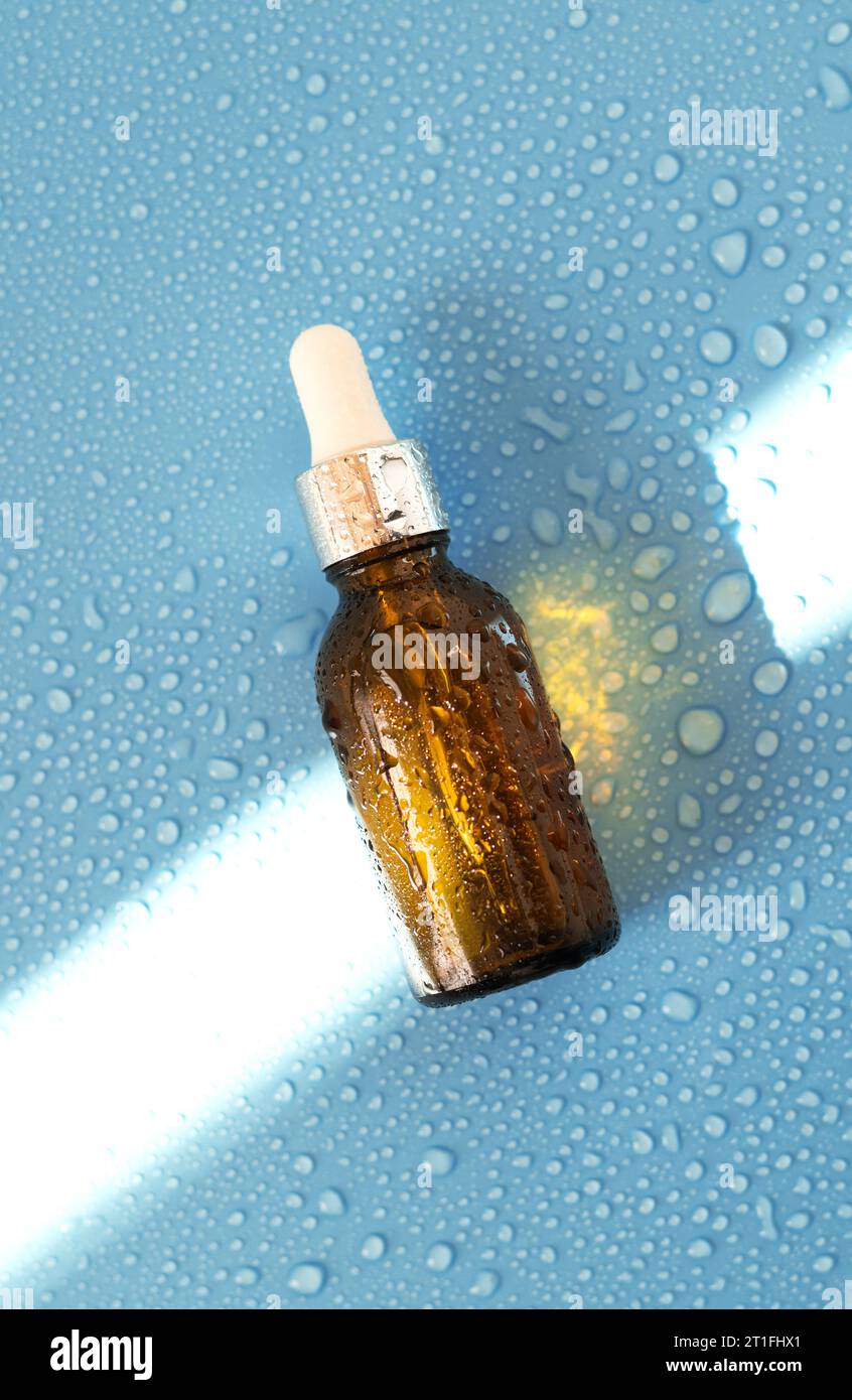 Flacone per siero , olio cosmetico su sfondo blu con luce dura e gocce d'acqua. con ombreggiatura piatta, vista superiore Foto Stock