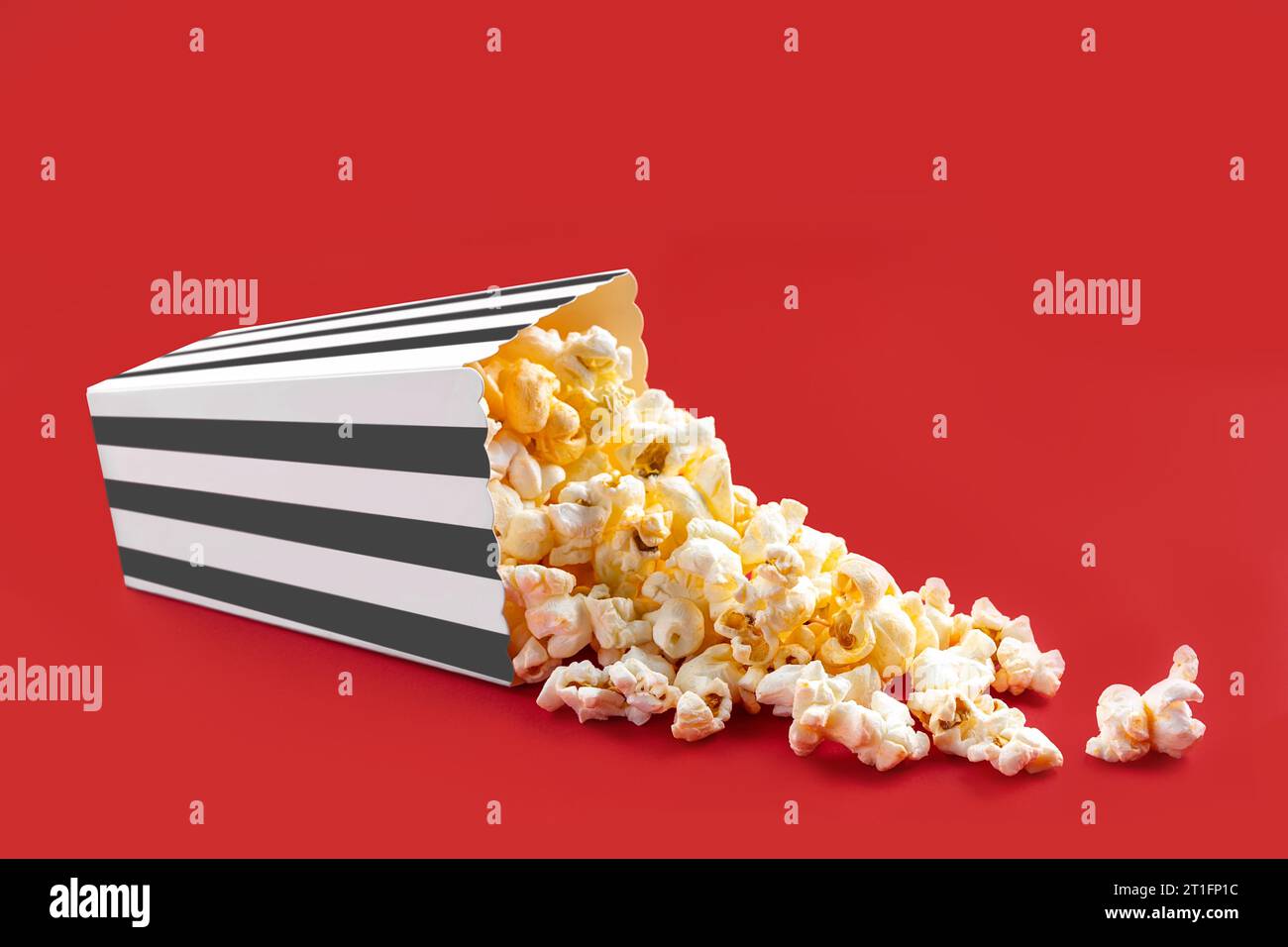 Gustosi popcorn al formaggio che cadono da una scatola di cartone a righe nere o da un secchio, isolato su sfondo rosso. Dispersione di semi di popcorn. Fast food, snack. Foto Stock