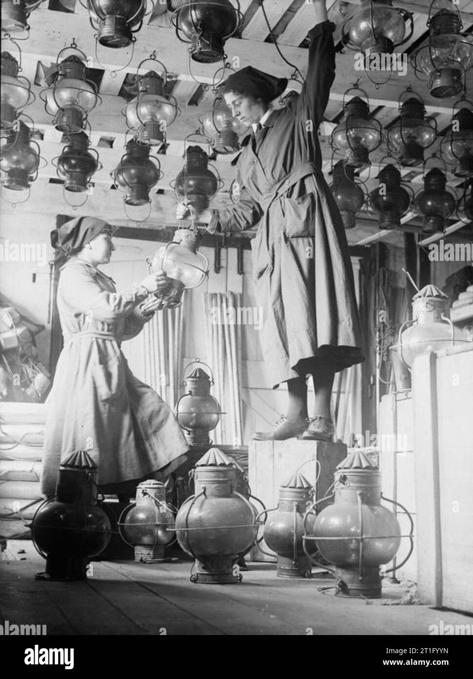 Donne in uniforme durante il primo mondo- Le donne del Royal Naval Service, Lowestoft, 1918 Un ritratto di WRNS store-donne al lavoro, ordinamento di navi" lampade in un ripostiglio a Lowestoft. Una donna si erge sul terreno e le mani una luce ad una seconda donna che si trova in piedi su una scatola rovesciata così che lei può appendere la luce con quelli già sospesi dal soffitto. Foto Stock