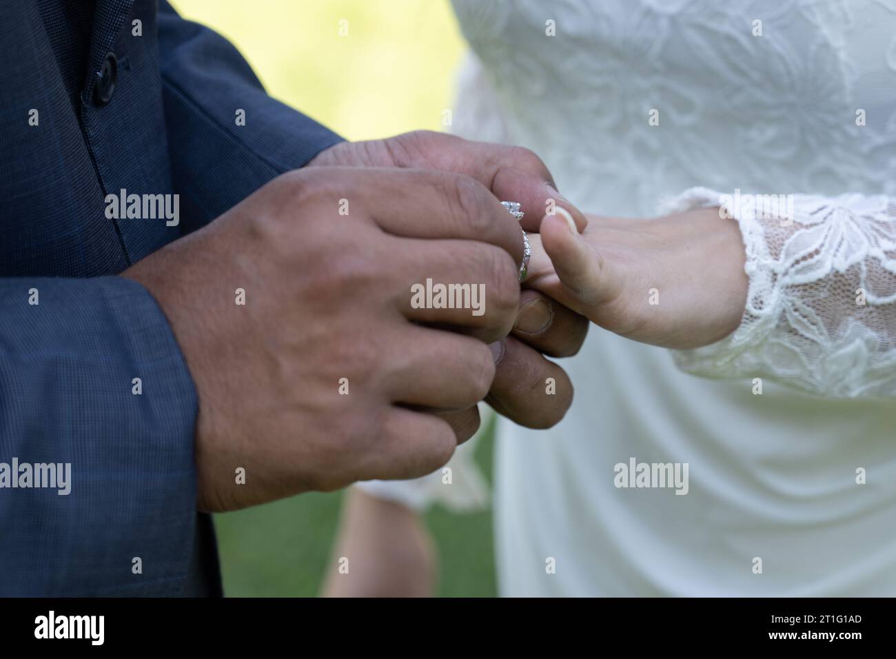 Le mani masoline dello sposo mettono l'anello nuziale sul dito della sposa come simbolo del suo impegno. Foto Stock