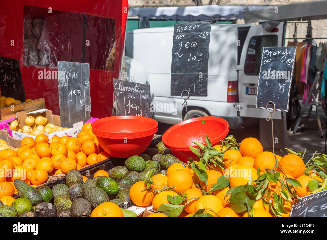Arance, avocado, pere e clementine in vendita nel mercato all'aperto del sabato ad Arles, Provenza, Francia meridionale. Ciotole di plastica rosse in primo piano. Foto Stock