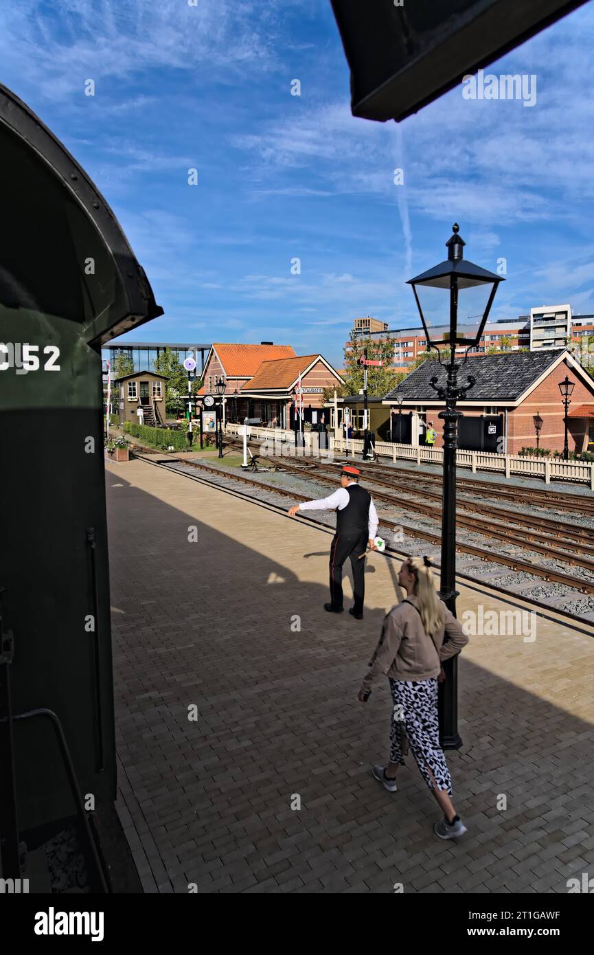 Partenza dal treno alla stazione, vista sul perron con un conducente vestito tradizionalmente guardia del treno, dipendente con cartello segnaletico nei Paesi Bassi Foto Stock