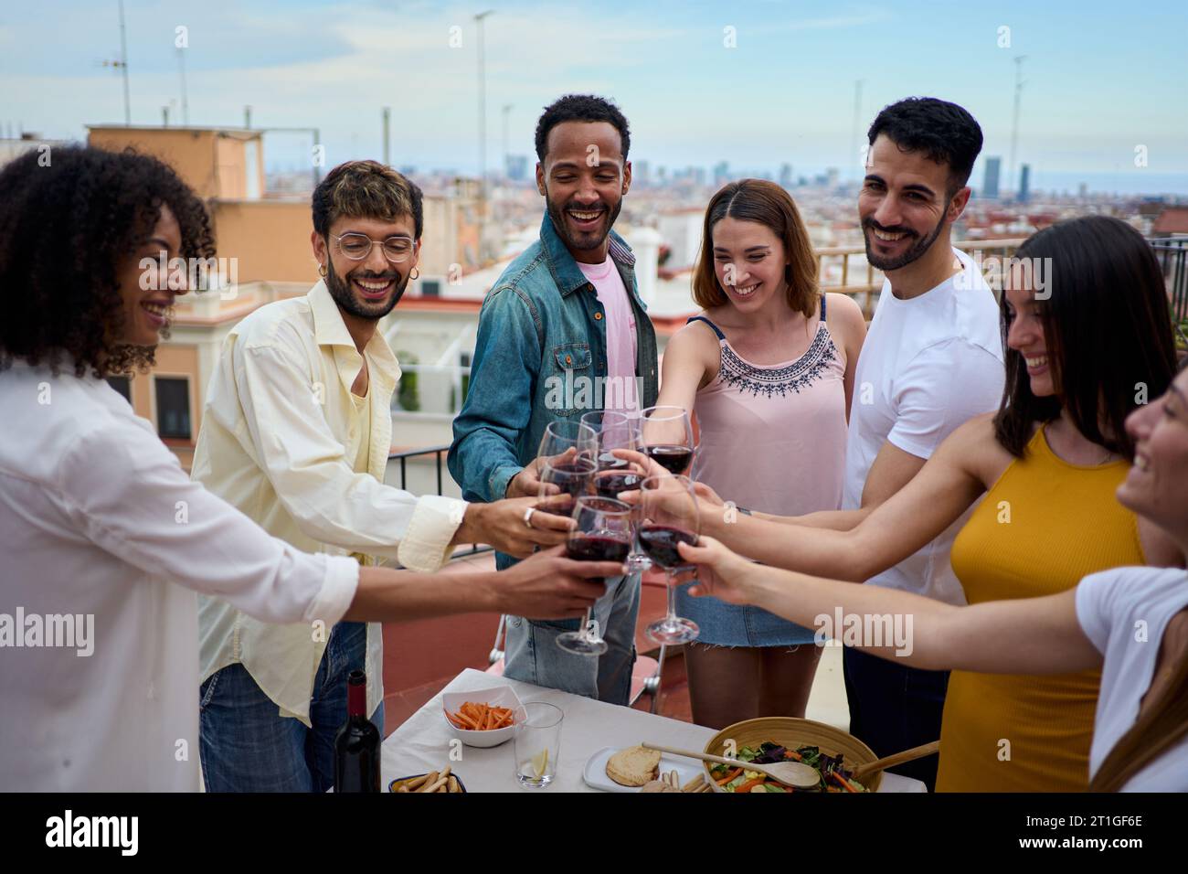 Sorridenti giovani multietnici che brindano bicchieri di vino in piedi per festeggiare i compleanni sul tetto. Foto Stock