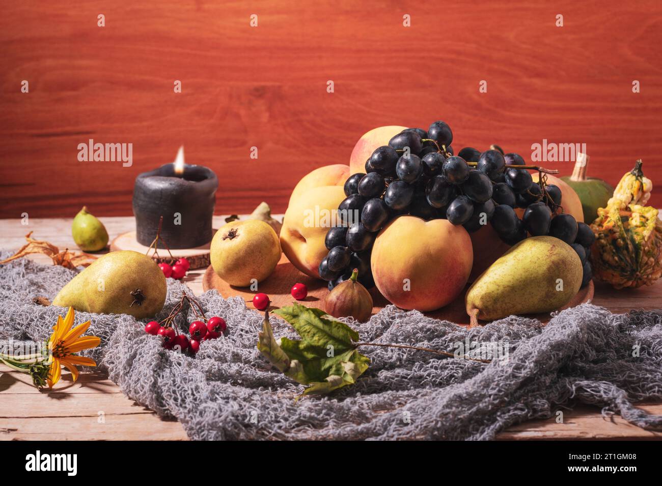 Natura morta autunnale con frutta, frutti di bosco, candele e foglie autunnali su fondo di legno. Foto Stock