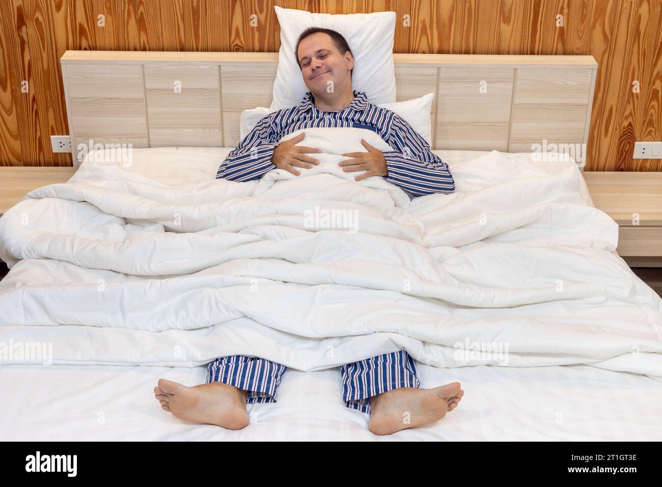 Un uomo in pigiama giace a letto con un'espressione beata sul viso Foto Stock