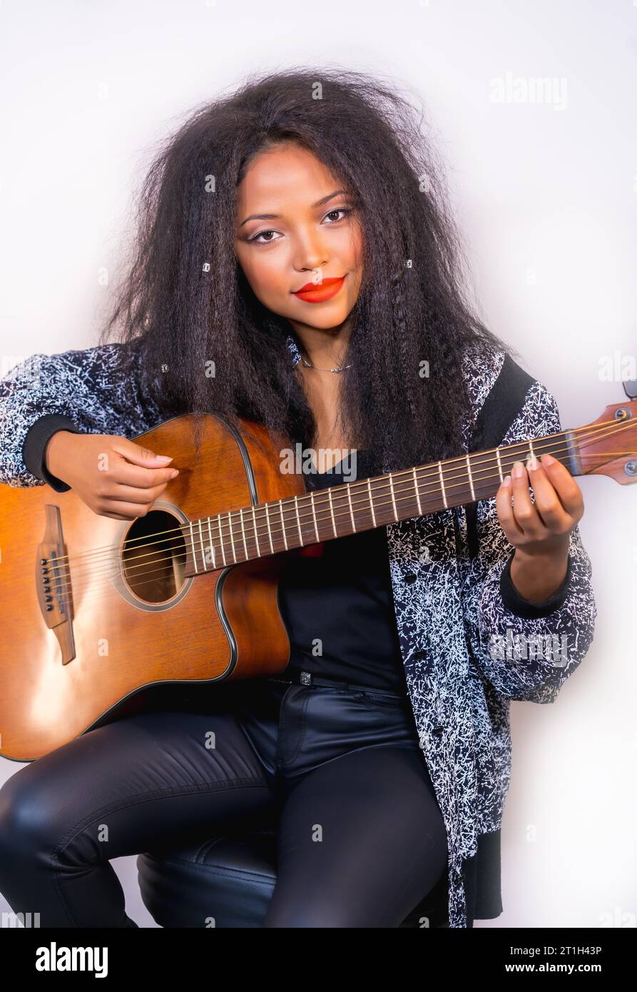 Un ritratto closeup di un'elegante e attraente musicista femminile che tiene una chitarra acustica sulla spalla Foto Stock