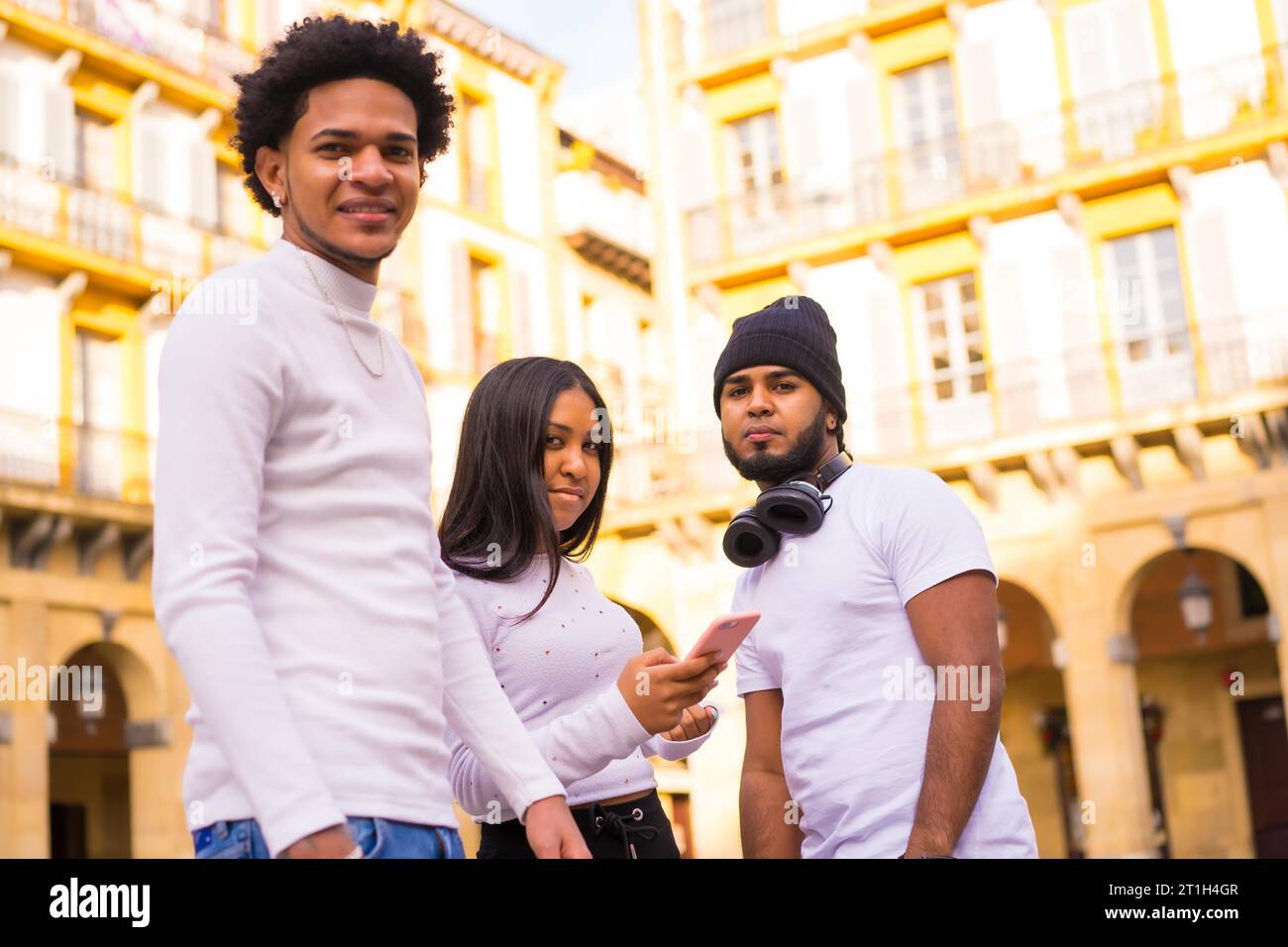 Stile di vita, amici latinoamericani neri che si divertono per strada con il telefono. Ragazzo afro-haired, giovane bruna e bruna bruna con capelli lunghi Foto Stock