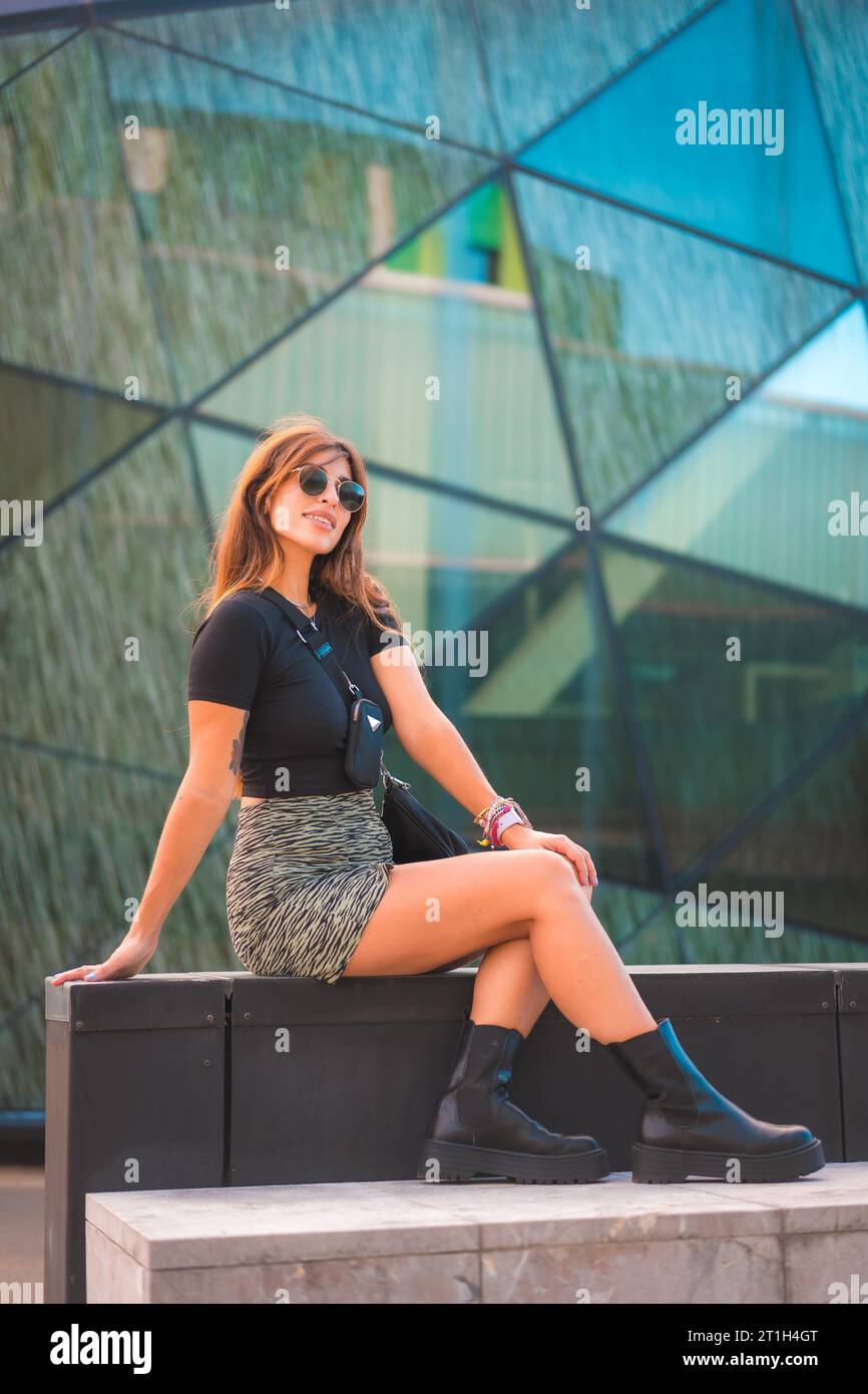 Stile di strada di un'attraente giovane bruna caucasica in città con occhiali da sole, in posa su splendidi cristalli verdi sullo sfondo Foto Stock