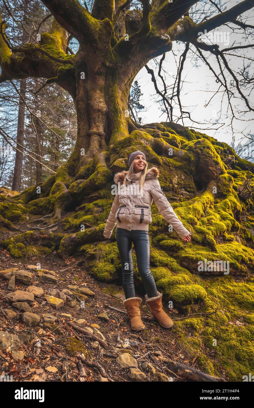 Parco naturale Gorbea, Bizkaia Spagna Â», Una bionda ragazza dai capelli diritti con una giacca di crema che visita il parco in un albero con muschio Foto Stock