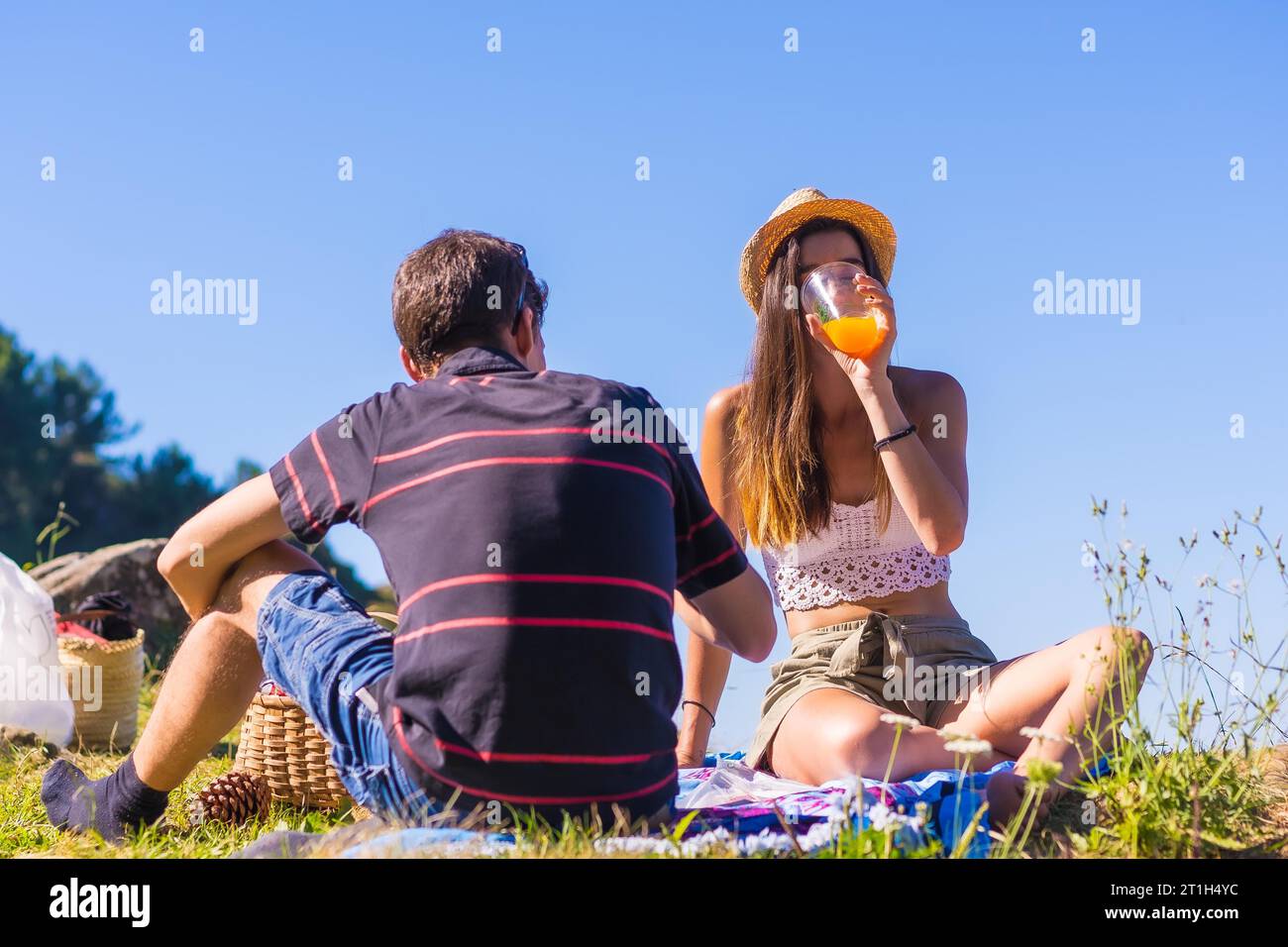 Una giovane coppia caucasica al picnic bevendo succo d'arancia in montagna vicino al mare godendo del caldo, stile di vita estivo Foto Stock