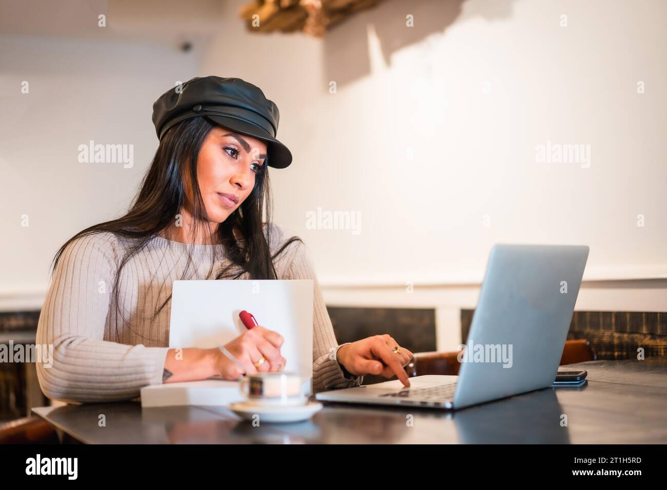 Bruna architetto latina che prende appunti durante una riunione online da un bar Foto Stock