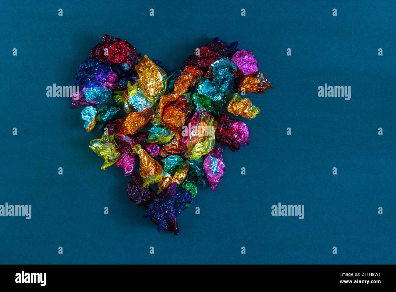 Involtini dolci al cioccolato multicolore disposti a forma di cuore su sfondo blu. Foto Stock