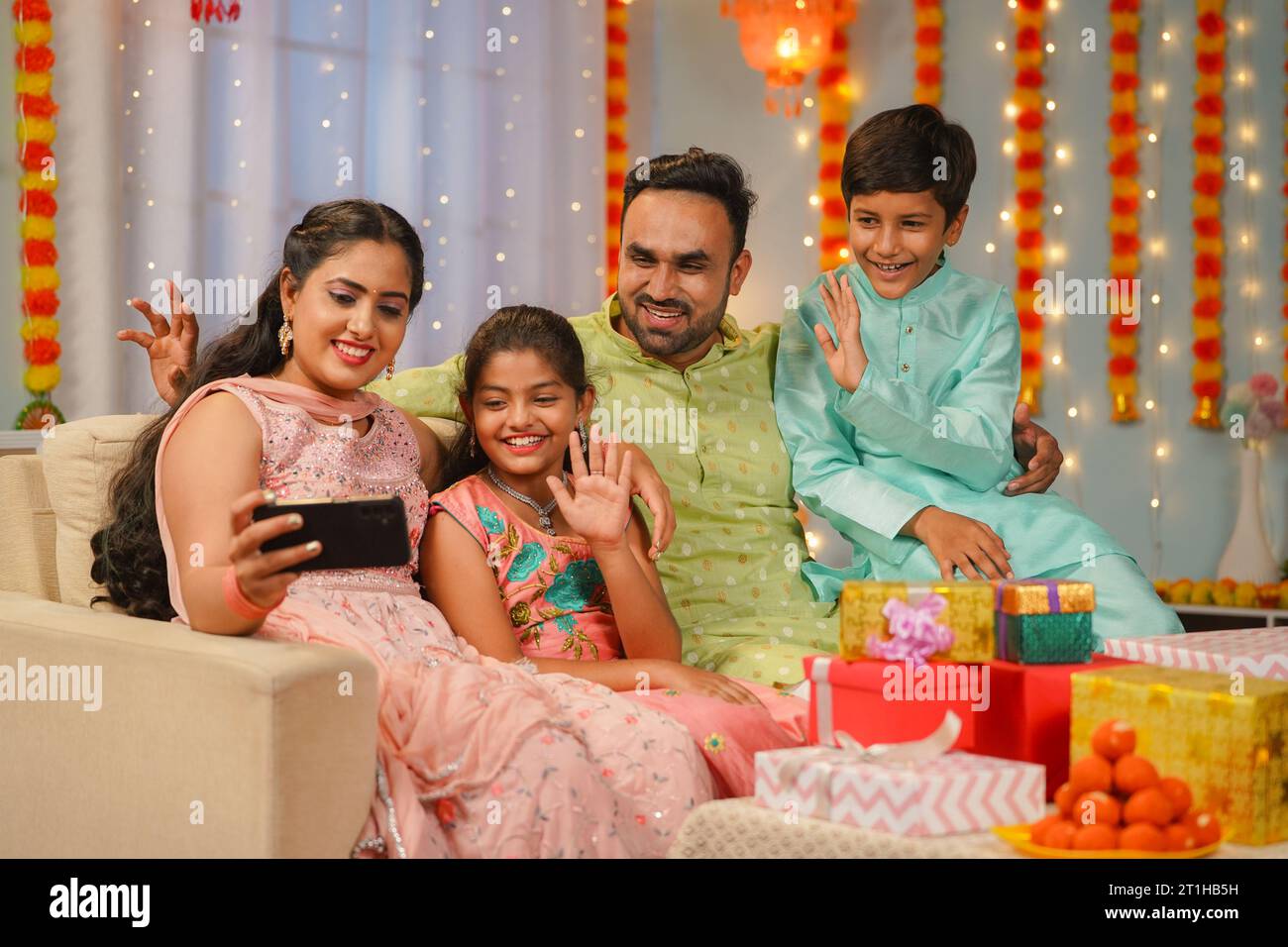 I giovani genitori felici con i fratelli che fanno videochiamate sul cellulare durante il festival diwali per i desideri a casa - concetto di festa Foto Stock