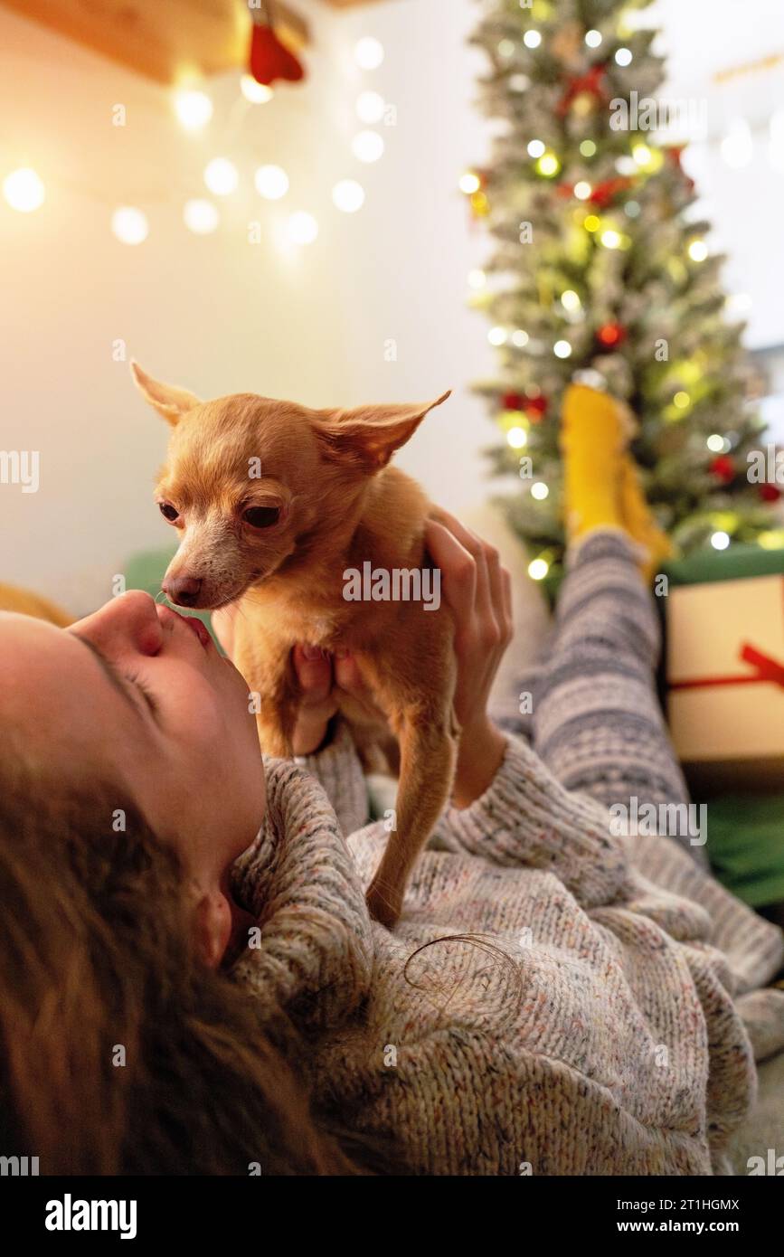 Amore e affetto per gli animali domestici. Donna sdraiata sul divano e baciata il suo cane da braccio durante il periodo natalizio. Foto Stock