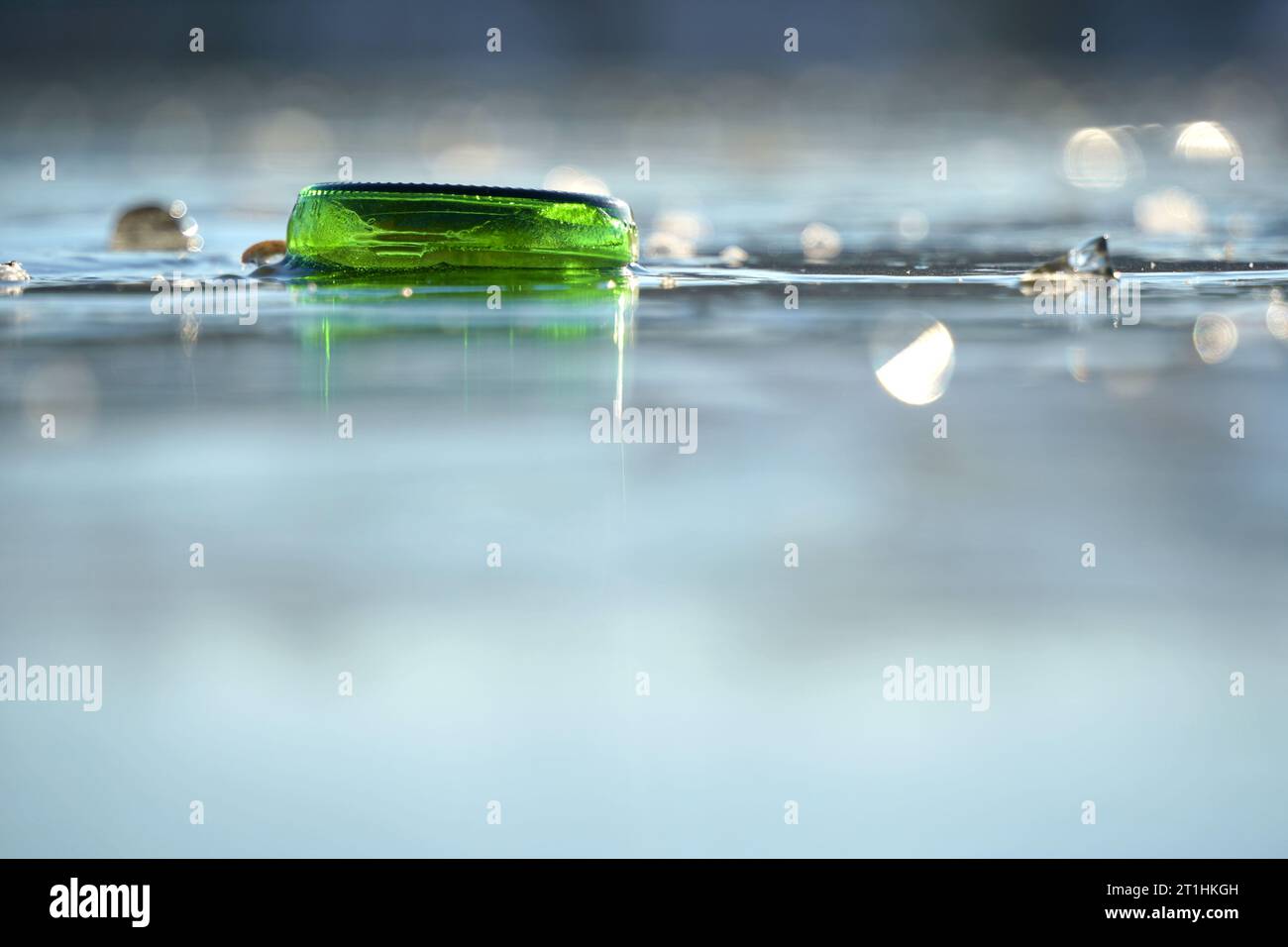 Il fondo della bottiglia verde è congelato solido nel lago. Piccole schegge di ghiaccio creano riflessi sulla superficie dell'acqua. Parte di un flacone. Vi. Anteriore Foto Stock