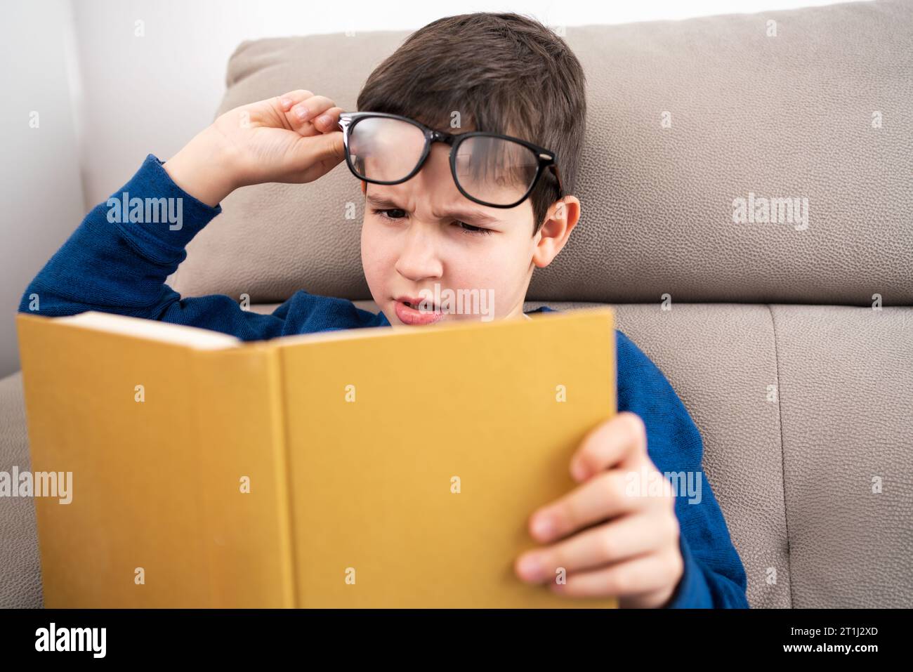 Bambino che soffre di affaticamento degli occhi che cerca di leggere un libro a casa Foto Stock