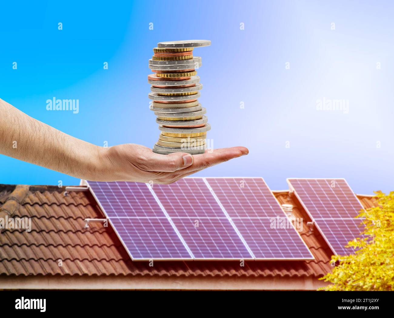 Pannello solare sul tetto della casa e monete in mano. Il concetto di risparmio economico ed energia pulita.risparmio di denaro Foto Stock