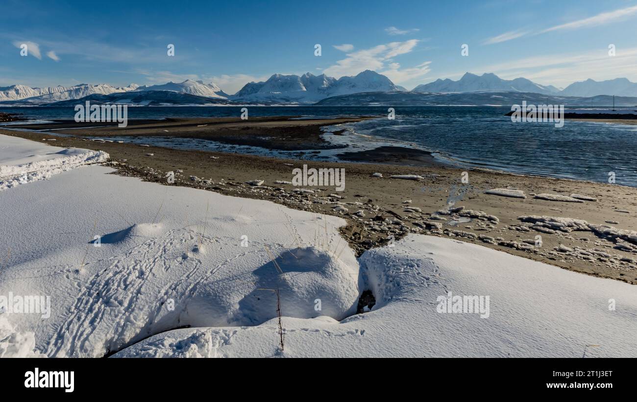 Una spiaggia innevata con montagne dietro il mare nel nord della Norvegia in inverno Foto Stock