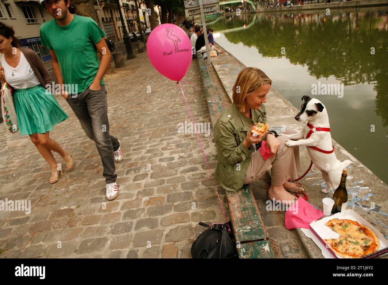 Una donna sta condividendo una pizza con il suo cane domestico sul lato di Canal St. Martin a Parigi, Francia Foto Stock