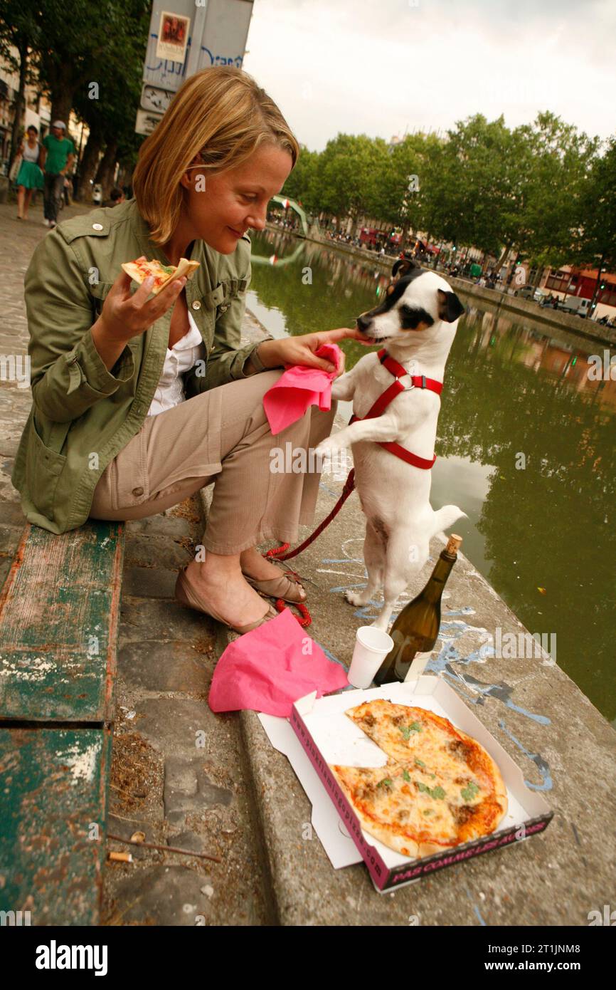 Una donna e il suo cane condividono una pizza, su Canal St Martin, Parigi Foto Stock