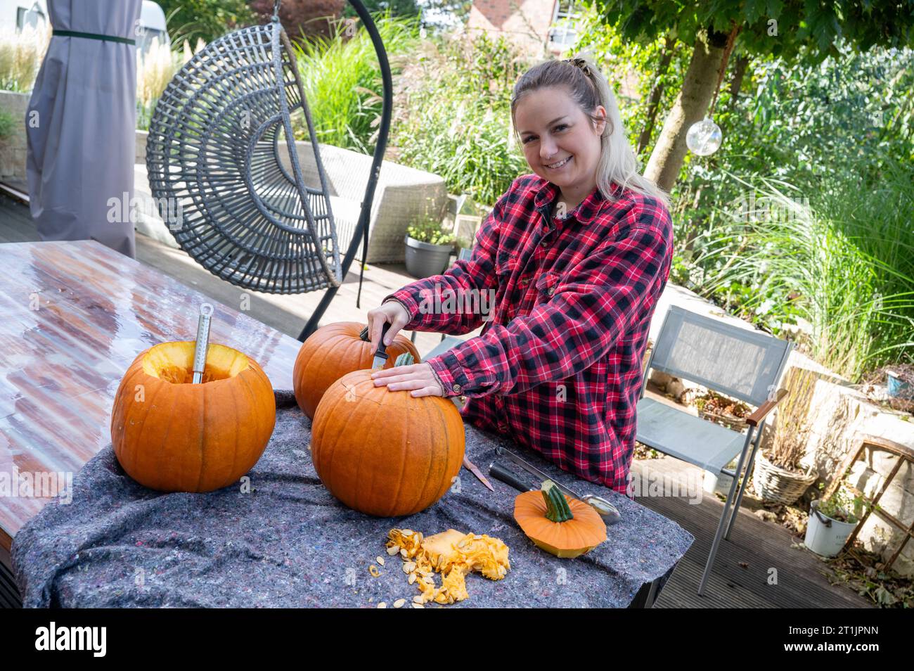 Donna bionda che apre la parte superiore di una zucca per intagliare le decorazioni di halloween con un coltello Foto Stock