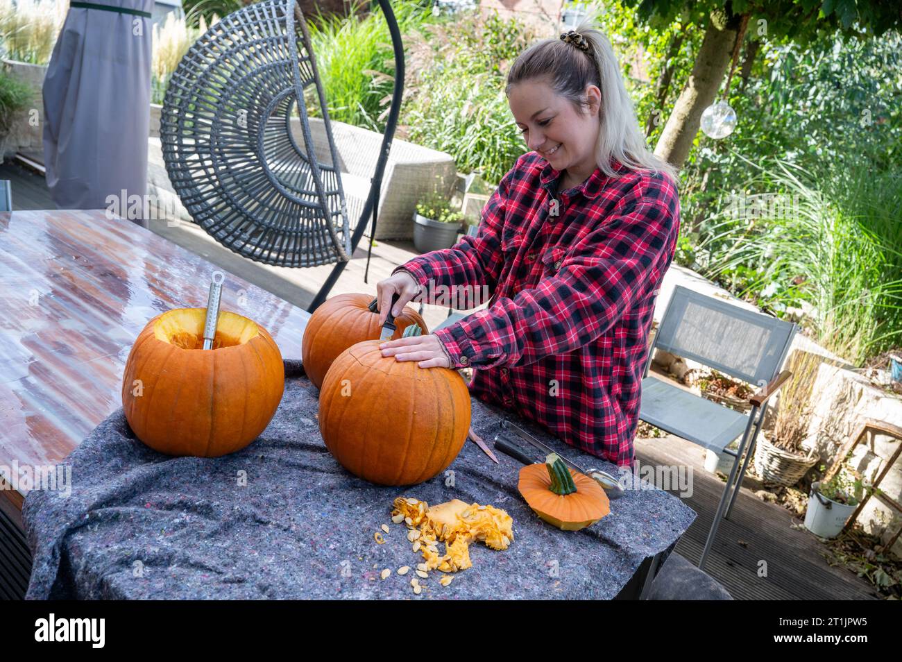 Donna bionda che apre la parte superiore di una zucca per intagliare le decorazioni di halloween con un coltello Foto Stock