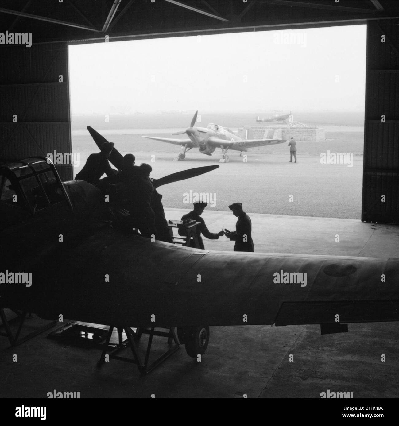 Royal Air Force Fighter Command, 1939-1945 aeromobili di n. 58 funzionamento unità di formazione a Grangemouth, Stirlingshire: un miglia marchio Master I subisce un servizio del motore nell'hangar, mentre un altro Master è parcheggiato sul disco in piedi al di fuori. In sottofondo un Supermarine Spitfire può essere visto taxying sul campo d'aviazione. Foto Stock