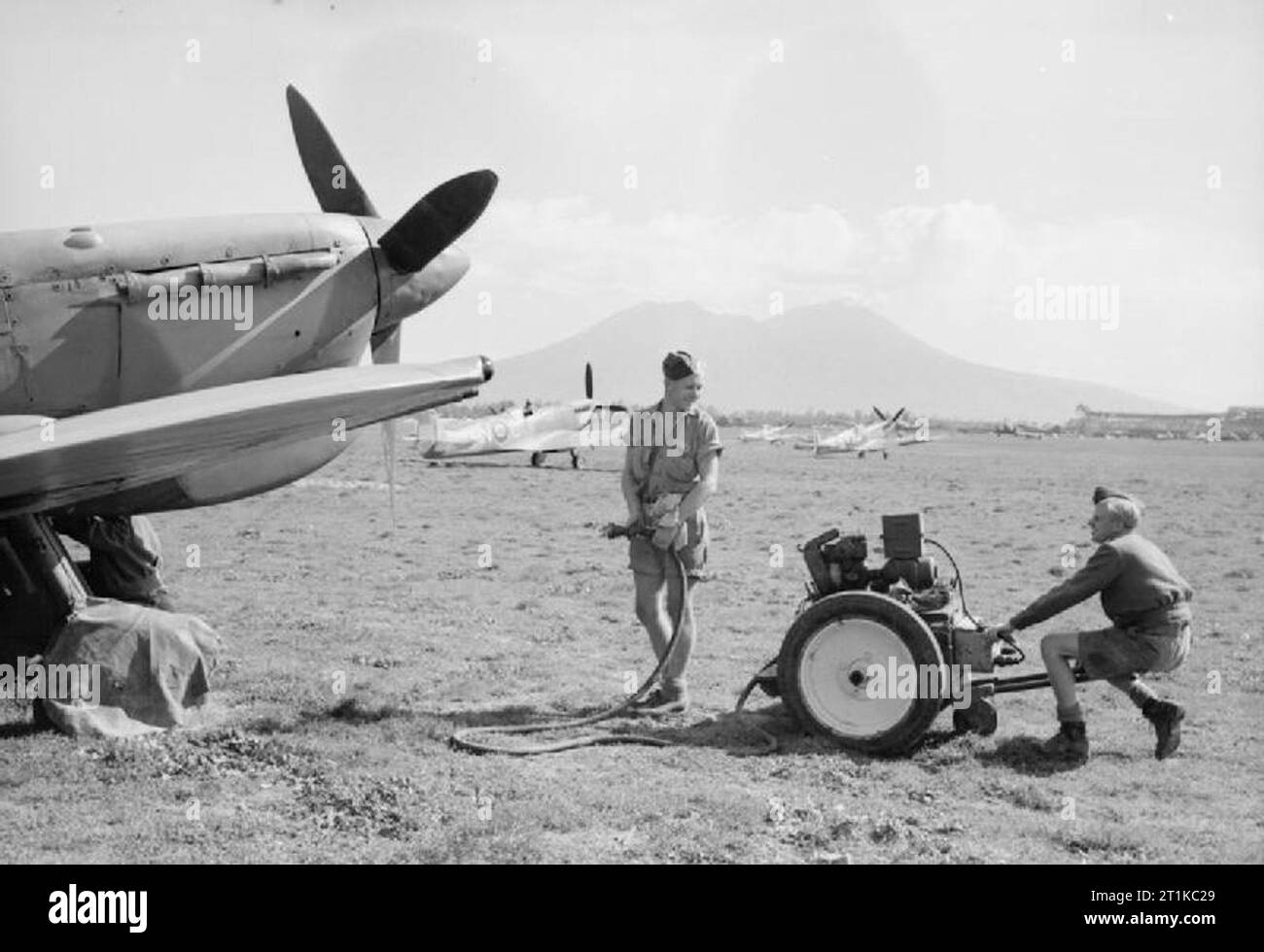 Royal Air Force - L'Italia, i paesi dei Balcani e del sud-est Europa, 1942-1945. Personale di terra preparare per avviare un Supermarine Spitfire Mark VC di n. 324 Ala RAF a Capodichino vicino a Napoli, utilizzando un carro-accumulatore. Spitfire Mark IXs di n. 93 Squadron RAF può essere visto parcheggiato in background, con il Vesuvio in lontananza. Foto Stock