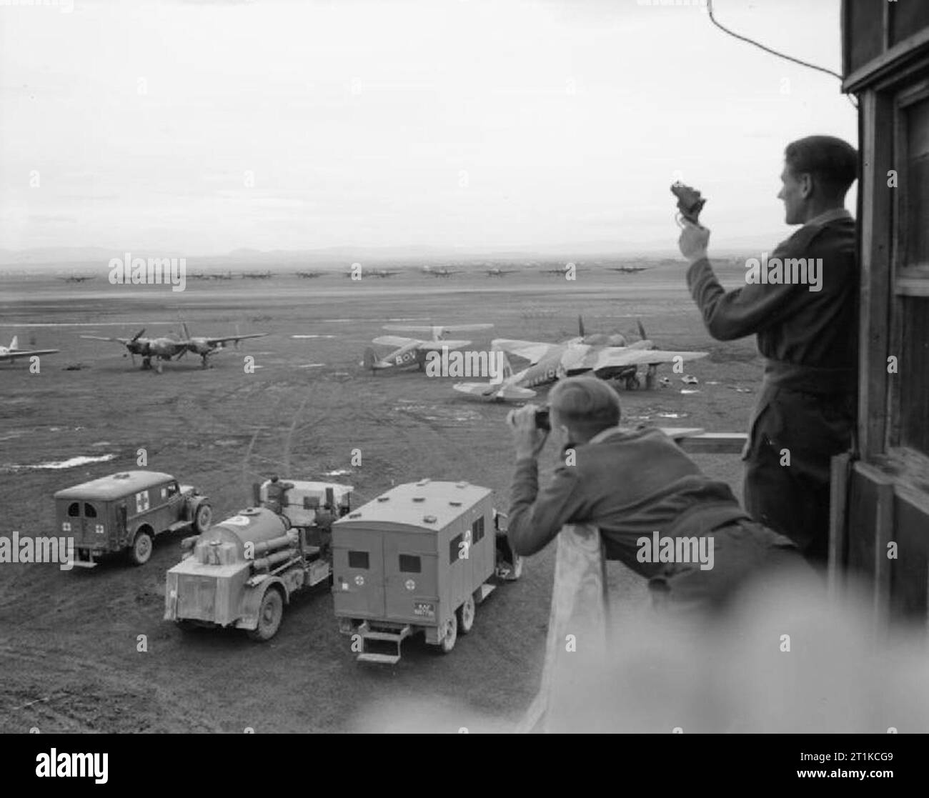 Royal Air Force- Italia,i Balcani e il sud-est Europa, 1942-1945. Una vista dall'orologio office a Foggia Main, l'Italia, come un aviatore si prepara a un incendio molto pistola dal balcone. Parcheggiato immediatamente al di sotto della torre sono due airfield ambulanze e un Crossley Fire Crash gara. Al di là dei veicoli sono un certo numero di visitare gli aeromobili, inclusi (da sinistra a destra): un Lockheed P-38 del XV USAAF; due comunicazioni di aeromobili, un Fairchild Argus del Medio Oriente squadrone di comunicazioni e un Vultee Stinson vigili e de Havilland Mosquito NF Mark XIII, MM567 "RO-A', di n. 29 Squadron RAF, unde Foto Stock