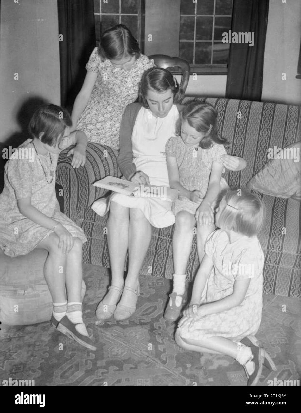 Isola di canale di sfollati provare su capi di abbigliamento americano in Marple, Cheshire, Inghilterra, 1940 Un gruppo di giovani ragazze evacuate dalle isole del Canale di Cheshire leggere e rilassarsi mentre indossano i vestiti donati a loro come doni da American ben wishers. Foto Stock