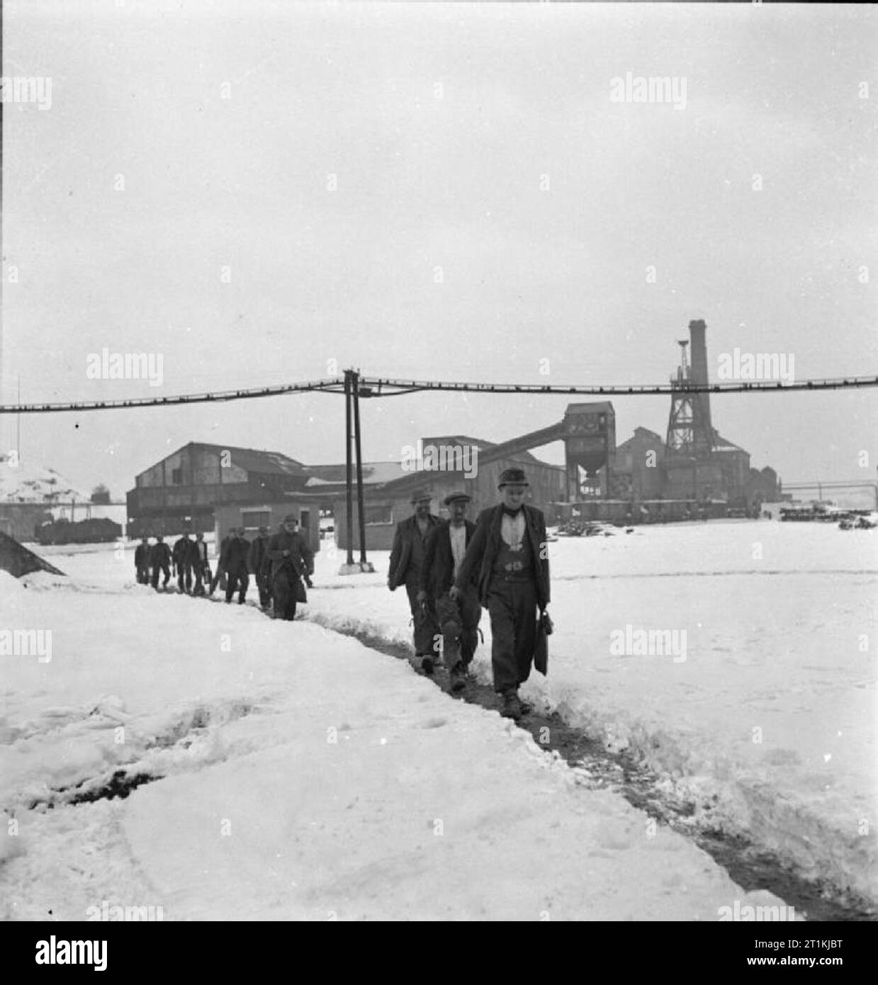 Miniere di carbone - La vita quotidiana in un Midlands Colliery, Inghilterra, Regno Unito, 1944 minatori in una miniera di carbone, da qualche parte nelle Midlands, trudge attraverso la neve a seguito della loro sette ore e mezza di shift sul loro modo di spogliatoi e benvenuto docce calde. La miniera di edifici, incluso il mio albero ingranaggio di avvolgimento, scivolo e camino. Foto Stock