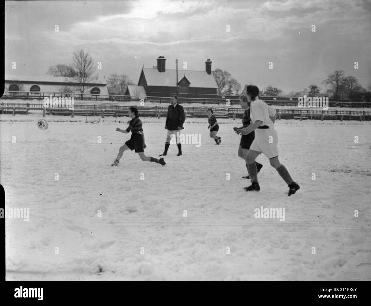 Faireys giocare a calcio- una donna Partita di calcio tra Fairey e Av Roe, Fallowfield, Manchester, Lancashire, Inghilterra, Regno Unito, 1944 Un giocatore sul Fairey team (indossare maglie a strisce) viene eseguito dopo che la sfera, come altri membri del suo team e di un giocatore dal AV Roe team dà la caccia. Chiaramente visibile tra l'azione sulla neve-coperta di passo è l'arbitro W H Dupois. La partita si svolge al Manchester Athletic Club la terra a Fallowfield. Foto Stock