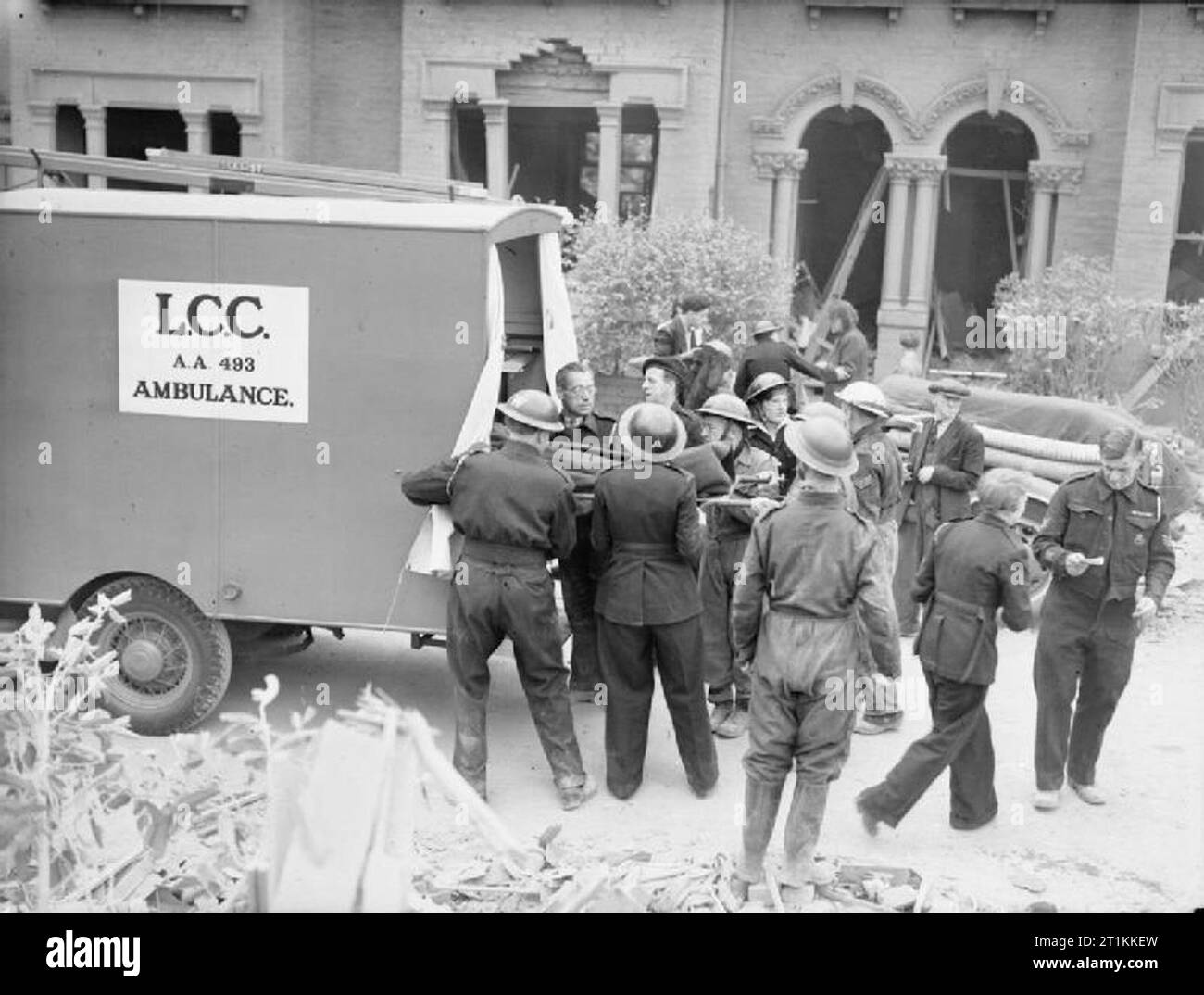 Flying Bomb- V1 danno della bomba a Londra, Inghilterra, Regno Unito, 1944 civili di difesa dei lavoratori aiutano il personale di ambulanza per il carico delle barelle in London County Council ambulanza a seguito di una devastante V1 attacco nella Highland Road e Lunham area di strada di Upper Norwood. Dietro di loro, i danni subiti dalle case su queste strade tranquille è chiaramente visibile: sono completamente senza porte e finestre. Foto Stock