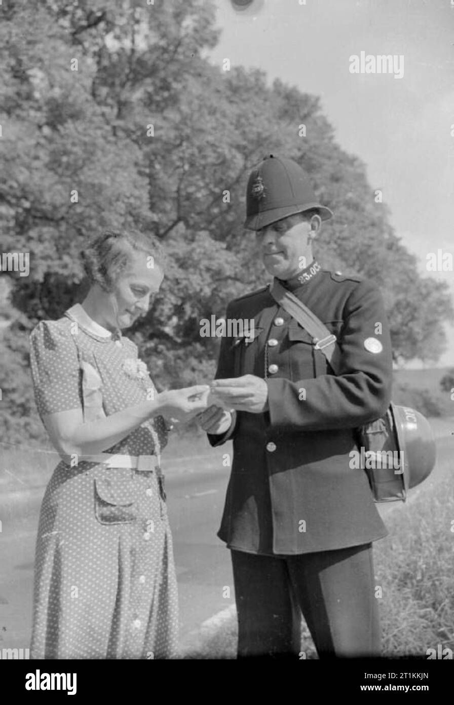 Un villaggio salva- Risparmio nazionale in Lewknor, Oxfordshire, Inghilterra, 1941 scuola di villaggio padrona, onorevole Scott, vende francobolli risparmio per il poliziotto locale, Hufton PC su un soleggiato vicolo del paese. PC Hufton è un ex-guardsman. Foto Stock