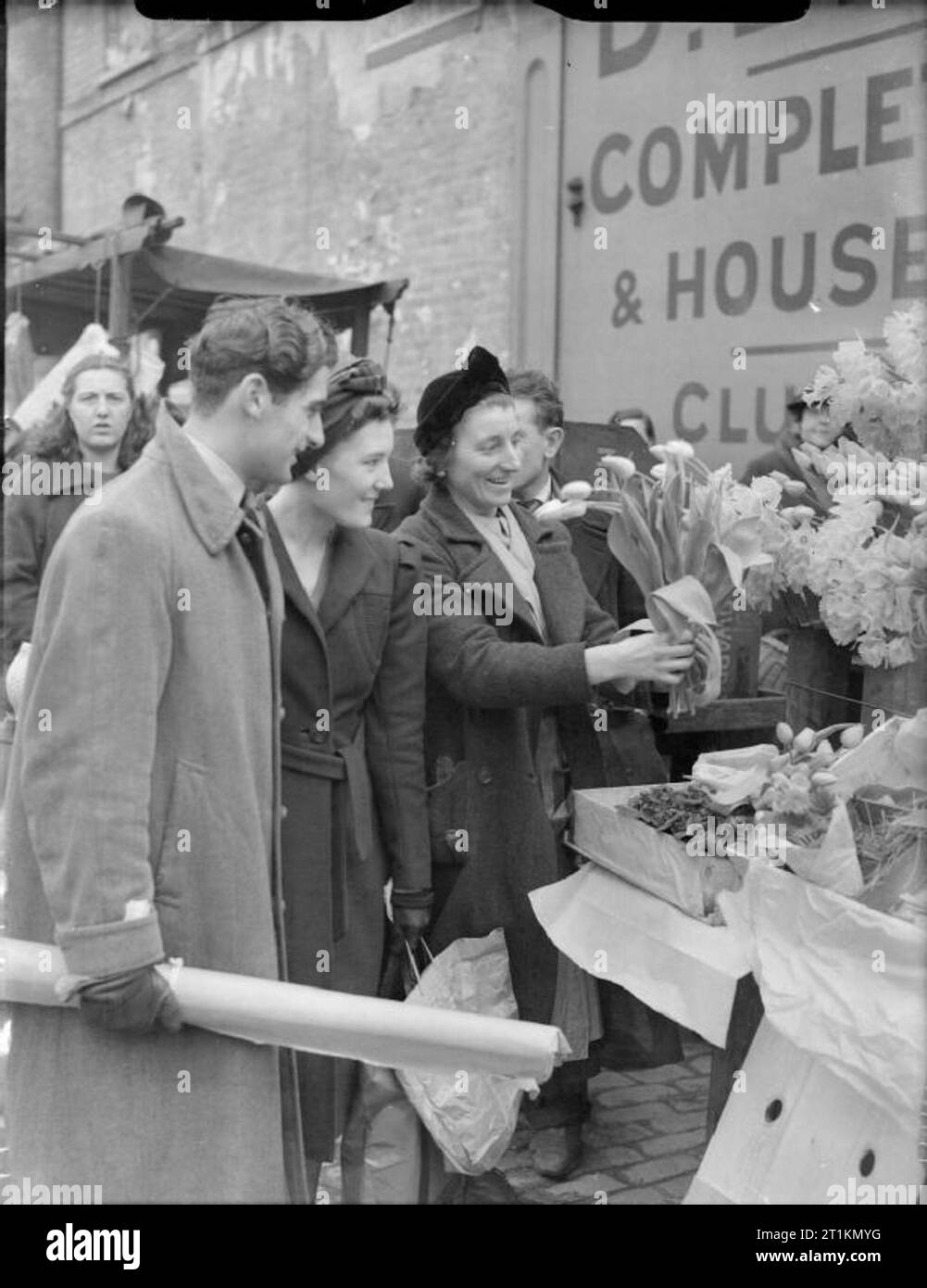 Londra in primavera del 1941- La vita quotidiana a Londra in Inghilterra un sorridente fiore-venditore vende fiori freschi dal Covent Garden a due felici i clienti che visitano il suo stallo a questo mercato di Londra. Così come i tulipani lei tiene, narcisi formano una grande parte della sua scorta. Foto Stock