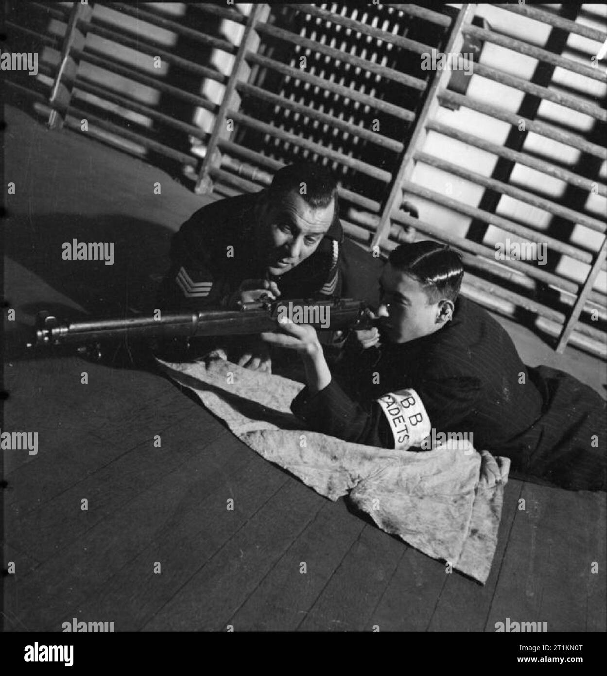 Gli ebrei di Londra in tempo di guerra - il lavoro di circoli giovanili in Stepney, London, 1942 Tenente Nat venditore, il ben noto boxing trainer, incarica il suo figlio Alfred nell uso di un fucile in palestra di Bernhard insediamento Baron boys' club su Berner Street, strada commerciale, a est di Londra. Nota Alfred's brassard, che dice "BB Cadetti'. Secondo la didascalia originale, questa è soltanto la seconda settimana che hanno addestrato con fucili a canna rigata. Foto Stock