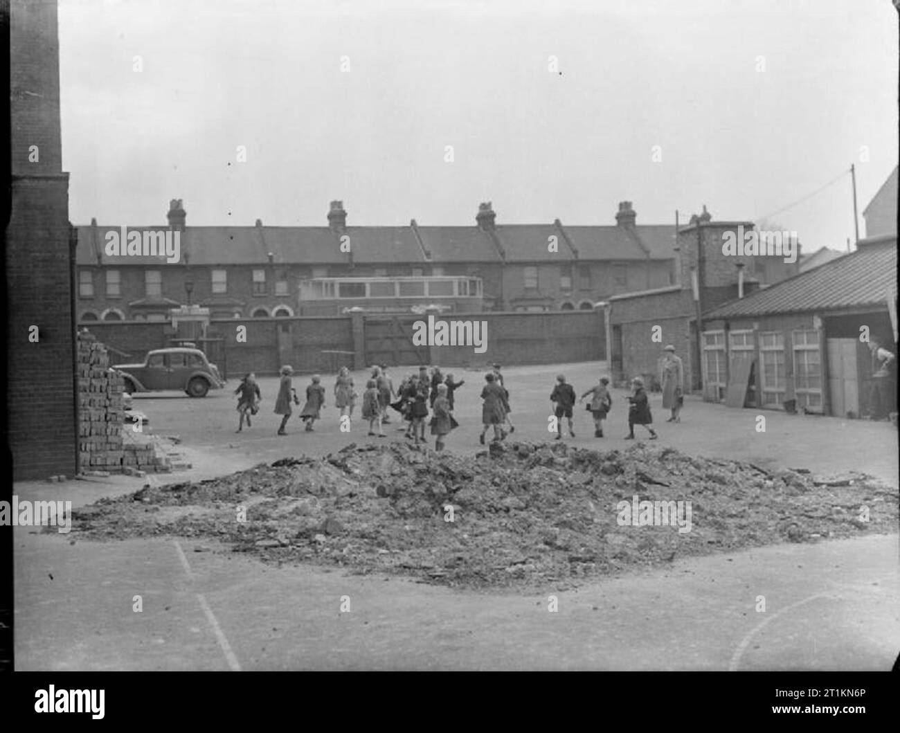 Scuole di Londra in tempo di guerra - La vita scolastica a Londra, Inghilterra, 1941 bambini, sotto la supervisione di un insegnante femminile, giocare nel parco giochi a parete lombardo scuola nel sud est di Londra. In primo piano una grande pila di macerie può essere visto, indicando che la scuola aveva sofferto di un qualche tipo di raid aereo. Foto Stock