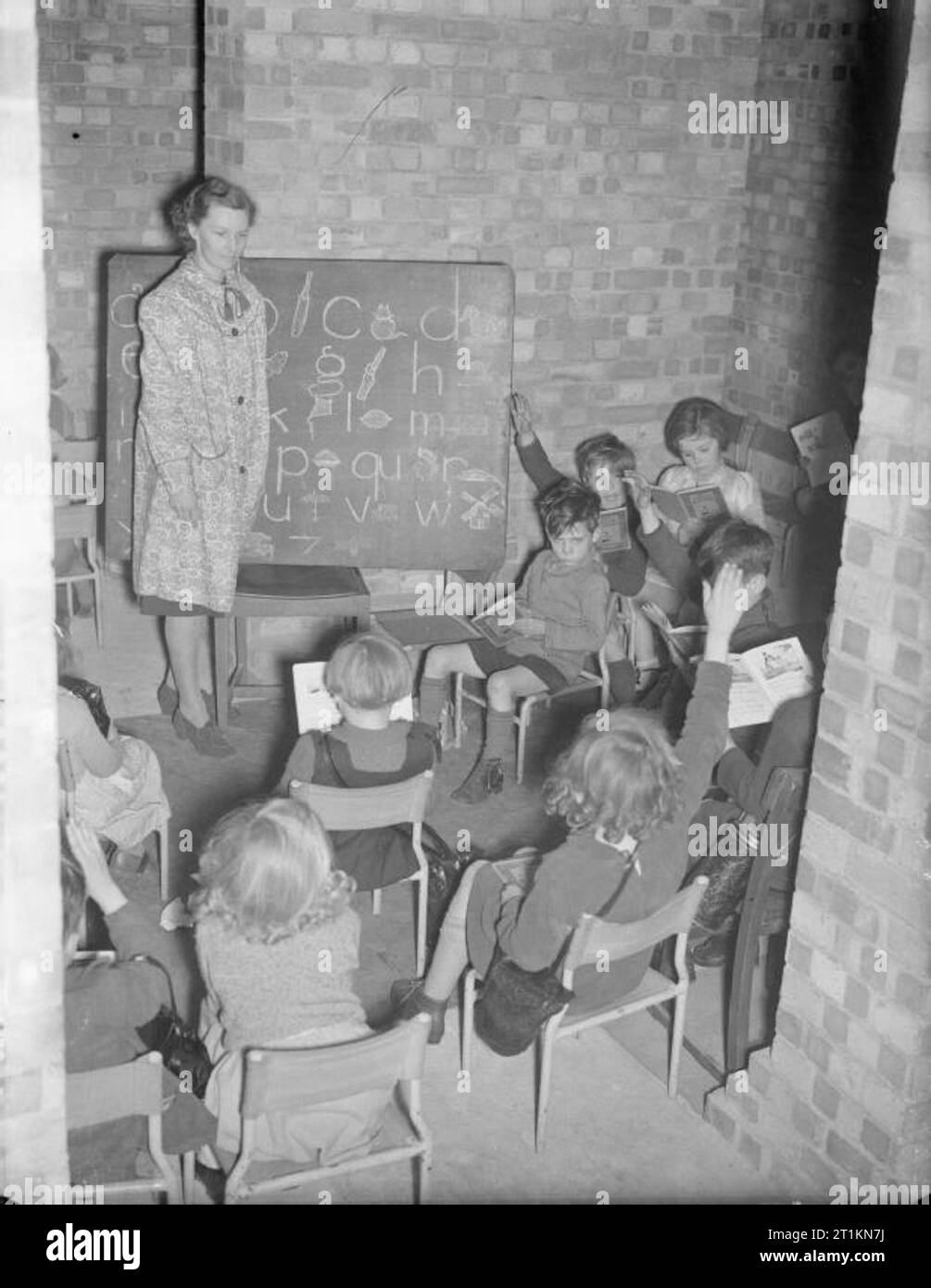 Scuole di Londra in tempo di guerra - La vita scolastica a Londra, Inghilterra, 1941 Un insegnante e i suoi studenti godono di una lezione in un seminterrato di strada Greco Scuola nel sud est di Londra nel 1941. Sulla lavagna, l'alfabeto è scritto e molti bambini hanno le mani sollevate, pronto a rispondere a una domanda. Anche se molte scuole sono state evacuate durante la guerra, molti hanno scelto di rimanere e 'make il meglio", conversione di cantine e seminterrati in Aule improvvisate. Foto Stock