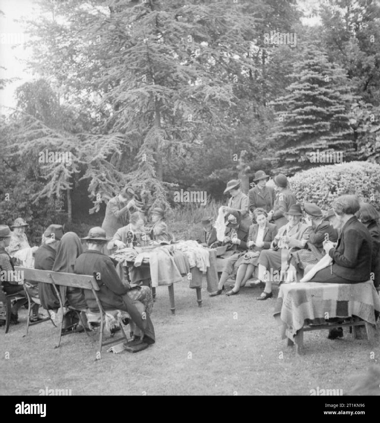 La commercializzazione senza soldi- abbigliamento per bambini Exchange, Norwood, England, Regno Unito, 1943 nelle belle giornate, la 'make-do-e-Mend' work party di Norwood Exchange tenere la loro riunione settimanale nel giardino della testa dello scambio, Onorevole Jenkins. Qui essi riparazione e ri-abbigliamento da lavoro che è stato portato in Exchange, creando nuove dal vecchio. Secondo la didascalia originale, questo include elbowless ponticelli essendo dipanate e ri-Prodotti lavorati a maglia ed una coppia di i pantaloni da uomo di essere trasformato in una piccola ragazza in tuta. Foto Stock