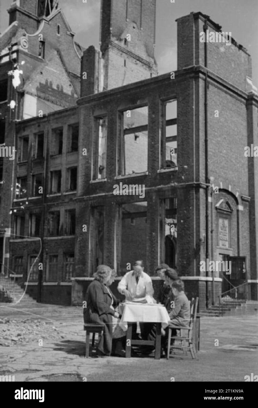 Aiuti dall America- Lend Lease cibo, Londra, Inghilterra, 1941 Un cameriere piatti su una piastra di American uova e pancetta per un gruppo di persone sedute a un tavolo al di fuori del guscio vuoto di una bomba gravemente danneggiato la scuola. La scuola ha le parole "ayer Street scuole, 1891' sulla lapide visibile sulla destra della fotografia. Questa fotografia è stata probabilmente preso a fine agosto o primi di settembre 1941. Foto Stock